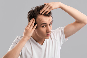 Young man with hair loss problem on grey background
