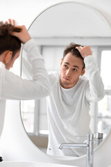 Young man with hair loss problem looking in mirror at home