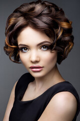 Fototapeta premium Glamour portrait of beautiful girl model with makeup and romantic wavy hairstyle. Fashion shiny highlighter on skin, sexy gloss lips make-up and dark eyebrows.