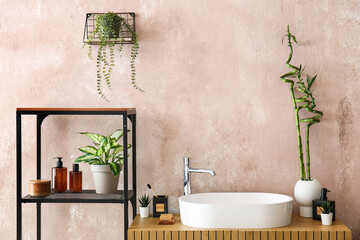 Sink, bath accessories and vase with bamboo stems on table in room