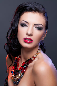 Beautiful brunette young woman with bright make-up and red lips wearing necklace. Copy space.