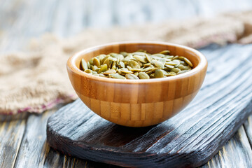 Pumpkin seeds in bowl on wooden board, selective focus.