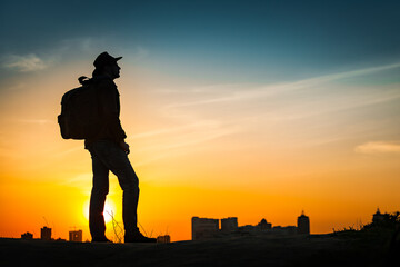 Traveler silhouette watching amazing sunset. Young casual man with backpack and cowboy hat standing...