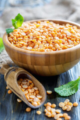 Wooden bowl with crushed yellow peas on the old table, selective focus.