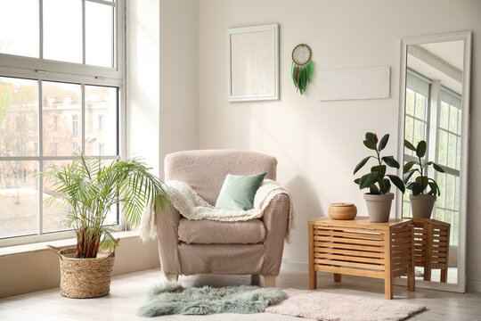 Interior of modern living room with armchair, plants and dream catcher hanging on light wall