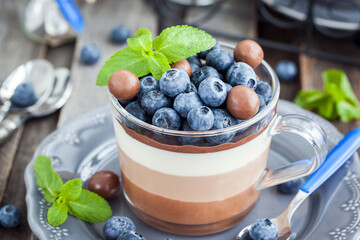 Delicious  three layered chocolate mousse dessert, devorated with fresh blueberry, mint and candies, served in glass cup