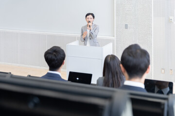 登壇してマイクを持って話すビジネスパーソン