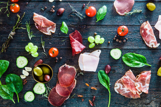 Italian ham, prosciutto and salami. Ingredients for bruschetta, crostini or sandwich bar. Rustic top view of ingredients. Ham with vegetables and spices