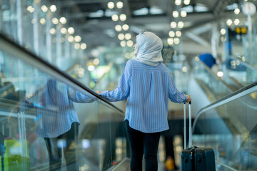 An Asian Muslim wearing a blue hijab is preparing for a vacation and she is at the airport. She is using her mobile phone to contact her friends and Muslim travelers.