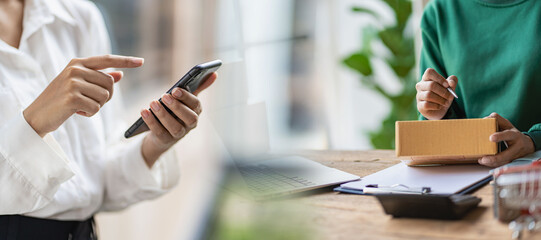 Small business start-up, SME, Asian female entrepreneur owner uses a smartphone or tablet to receive and verify online orders to prepare boxes for delivery of orders.