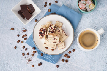Pieces of tasty marble halva and cup with coffee on light background