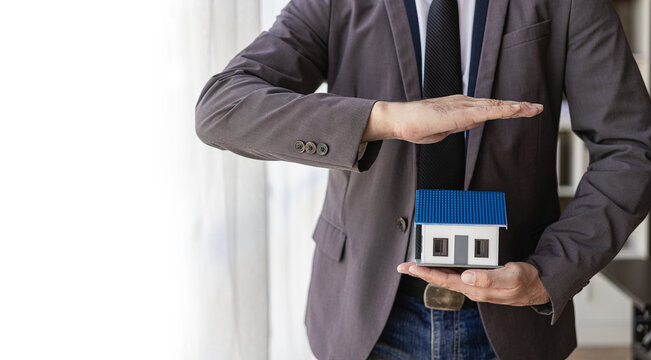 Businessman holding a small house in hand, small house insurance concept. Blue