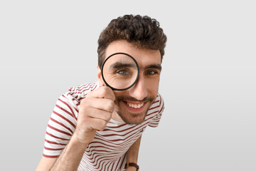 Young man looking through magnifier on light background, closeup