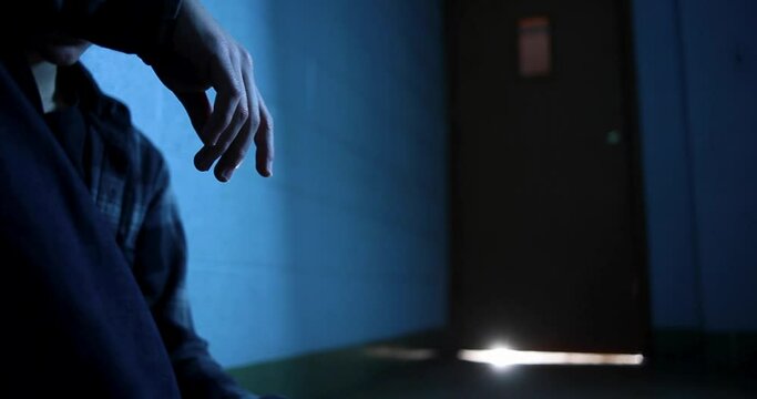 Camera dolly from a ray of light under a door to a sad teenager with hanging hand.