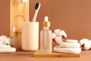 Bottles of essential oil, toothbrush, spa stones and cotton flowers on color background