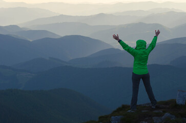 Woman with outstretched hands in mountains. Woman looks at mountains ranges. She is happy.