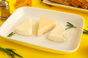Plate with triangles of tasty processed cheese on yellow background