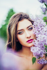 Portrait of young beautiful woman posing among lilac flowers. Professional make-up and hairstyle. Perfect skin. Fashion photo. Natural beauty. Springtime.