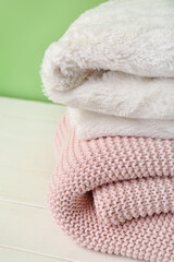 New soft folded blankets on light wooden table new green wall, closeup