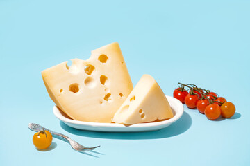 Plate with pieces of Swiss cheese and tomatoes on blue background