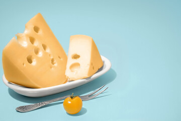 Plate with pieces of Swiss cheese and tomato on blue background