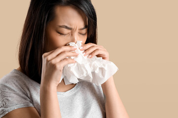 Ill Asian woman with tissues on beige background, closeup