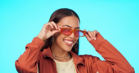 Woman, face and sunglasses for fashion for wink, smile and confidence with flirt, choice or style blue background. Girl, model and gen z student in designer eyewear, frame and lens for healthy vision