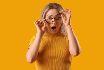 Surprised young woman in stylish eyeglasses on orange background