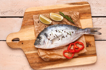 Board of raw dorado fish with lime and rosemary on light wooden background