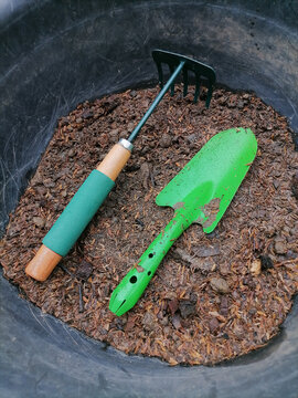 Green gardening tools are shovels and rakes placed in the soil pan. The background image is trees, leaves, lawns.