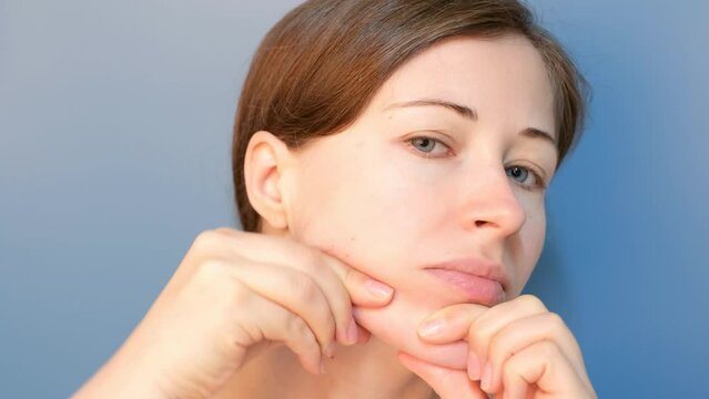 Young woman do self-massage of the face close-up on blue background.