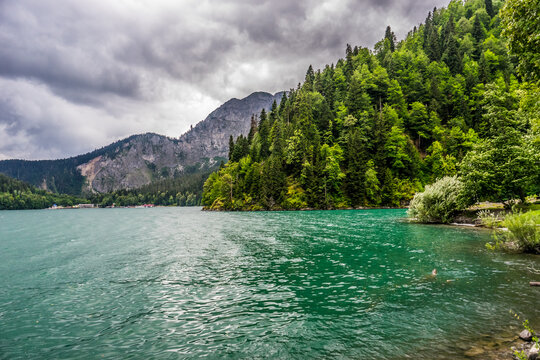 The emerald green lake framed by the forest and mountains in the gloomy rainy weather