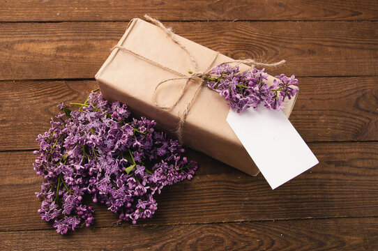 Bouquet of lilacs on a wooden table with a gift box of kraft paper with a label for the inscription