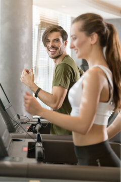Determined young man smiling while running on treadmill during high-intensity interval training
