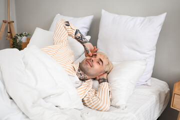 Young tattooed man waking up in bedroom