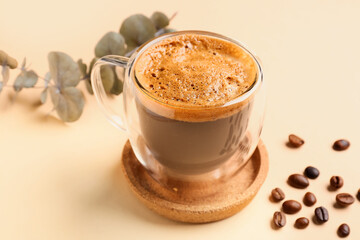 Glass cup of hot espresso and coffee beans with eucalyptus on beige background