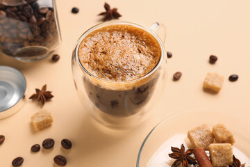 Glass cup of hot espresso and jar with coffee beans on beige background