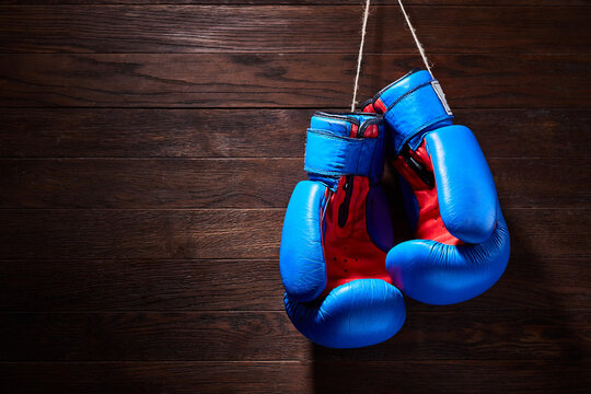 A pair of bright blue and red boxing gloves hangs against wooden background. Boxing backgrounds and still-life. Colorful accessories for sport. Horizontal photo. Training and sportive exercise. Concep