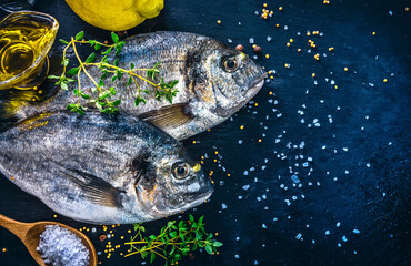 Fresh fish dorado top view. Spicy herb and vegetables healthy food spice on black stone board cooking. Copyspace.