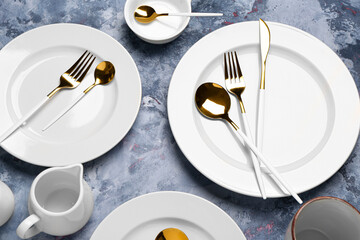 Clean plates with set of golden cutlery on blue grunge table