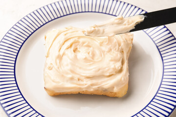 Plate of tasty toast with cream cheese on light background