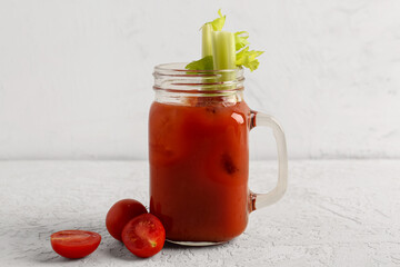 Mason jar of bloody mary with celery and tomatoes on white table