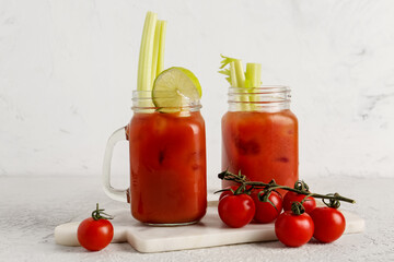 Mason jars of bloody mary with celery and tomatoes on white table