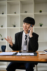 A smart Asian businessman is on the phone with his client, dealing business over the phone
