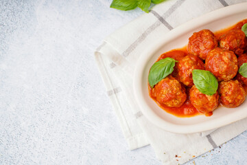 Plate of tasty meat balls with tomato sauce and basil on grey table