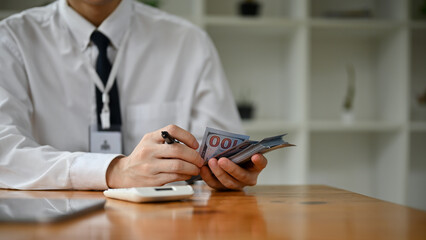 Fototapeta premium Close-up image of a professional Asian male banker counting US dollar bills at his desk