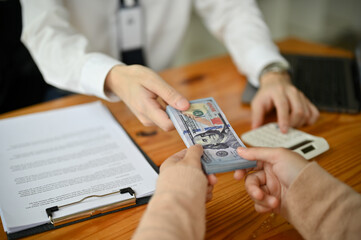 Close-up image of a professional male banker giving a wad of US dollar bills to a female customer.