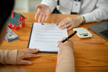 A female client signing her signature on an agreement document in front of a real estate agent