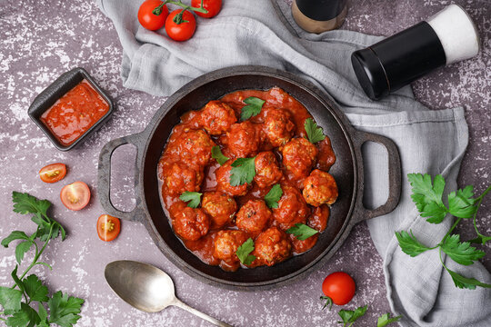 Frying pan of tasty meat balls with tomato sauce and parsley on grey background
