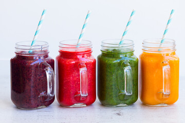 Colorful smoothie drinks in glass jars on white table close up